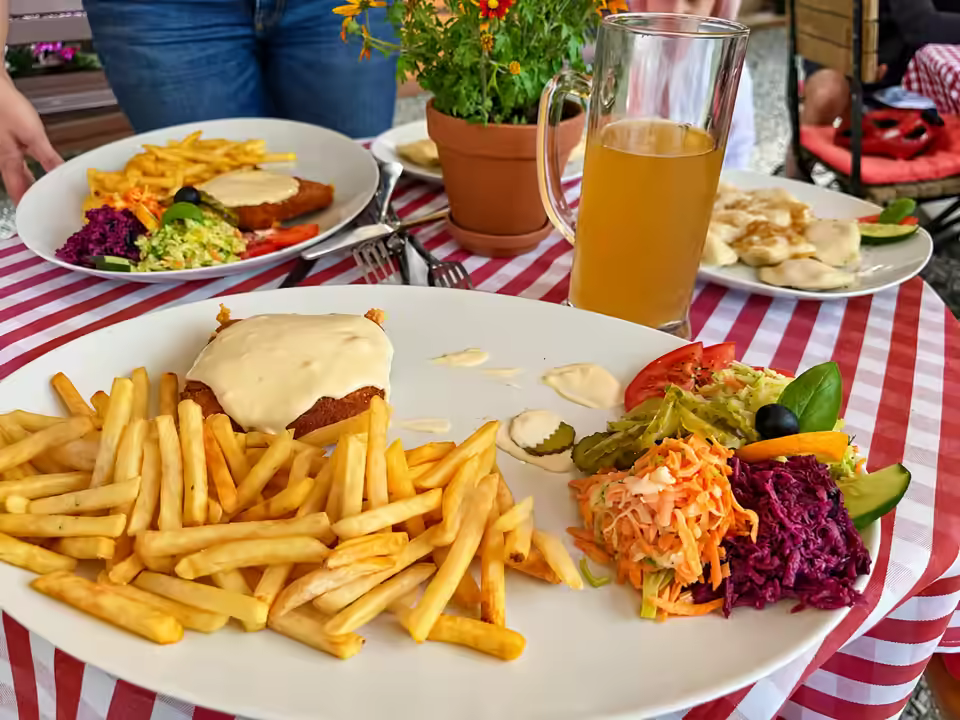 Kotlet z frytkami i surówką, obok kufel piwa i pierogi na stole w czerwoną kratę
